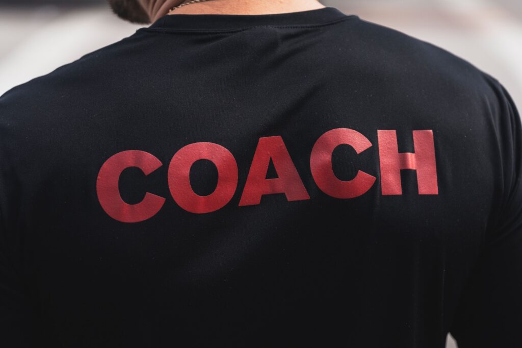 Close-up of a young man wearing a black t-shirt with the word 'Coach'